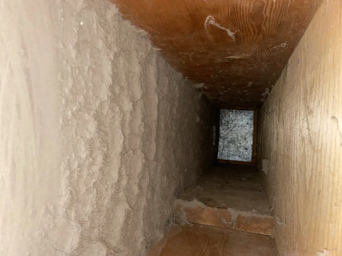 BEFORE air duct cleaning: wood plenum packed with thick grey dust and debris