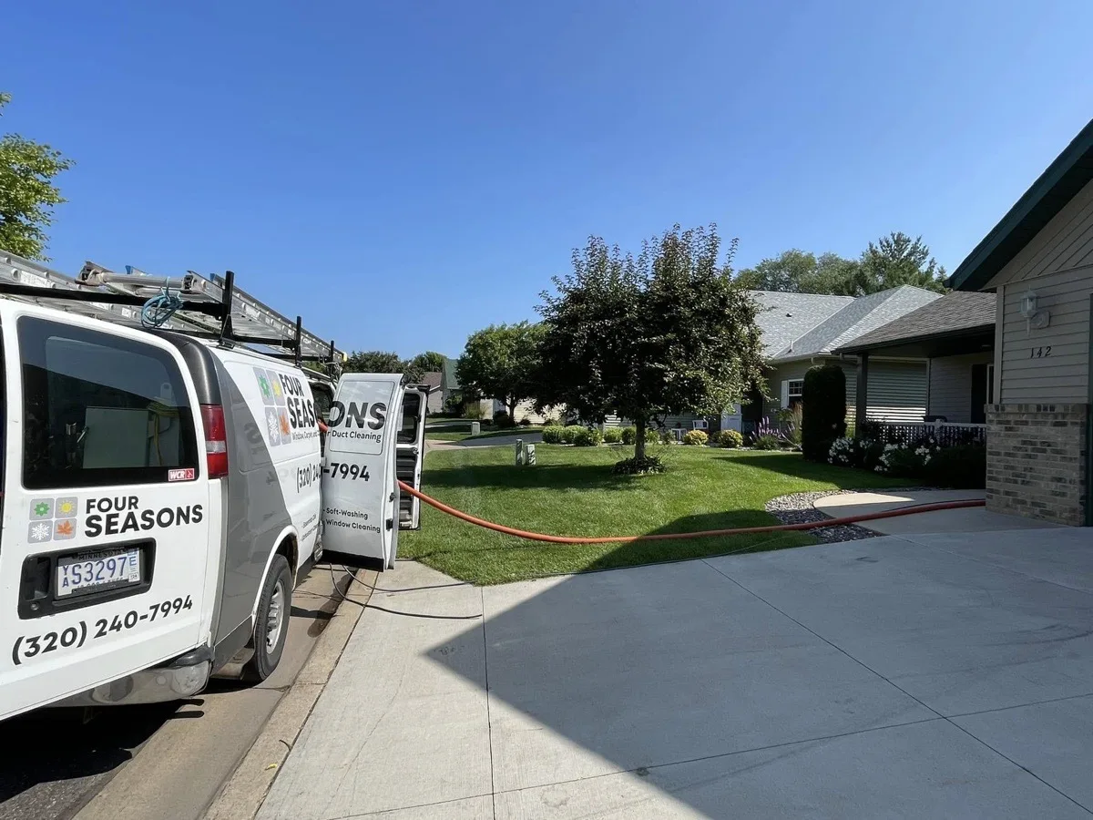 Four Seasons white service van parked at a residential driveway with equipment hose deployed