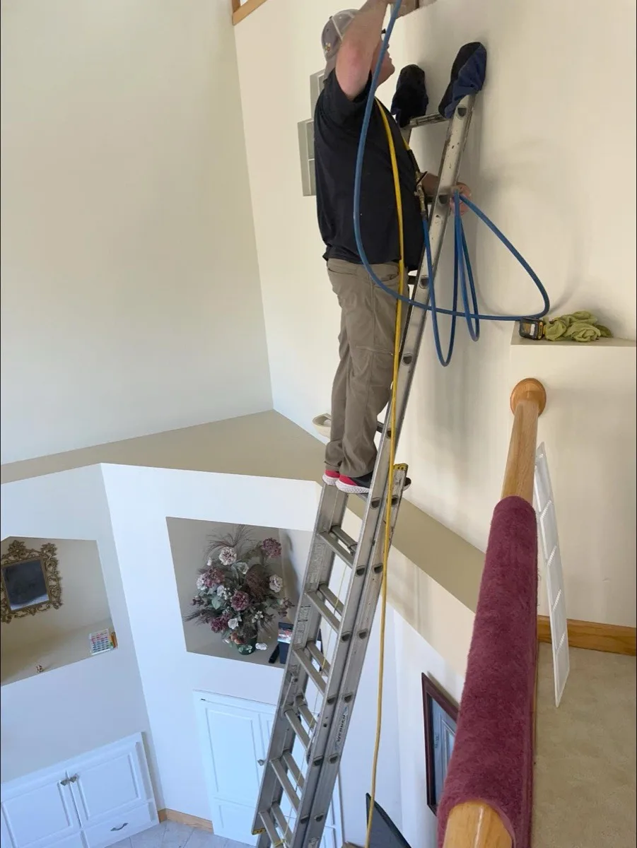 Matt Bertsch on a ladder performing air duct cleaning inside a customer's home