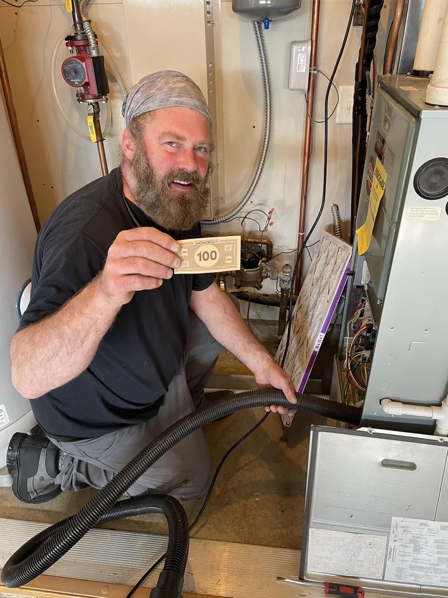 Technician grinning after finding Monopoly money hidden inside a residential air duct