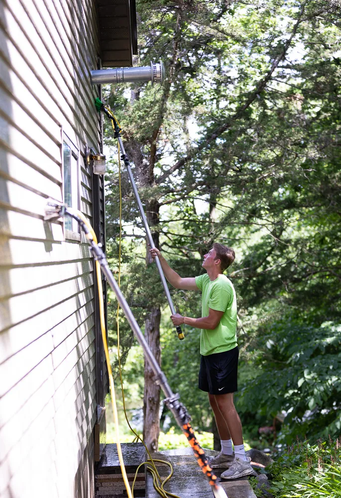 Four Seasons technician using a water-fed pole to soft wash upper siding and soffit of a residential home