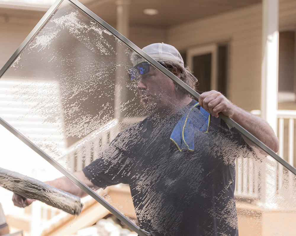 Four Seasons technician hand-scrubbing a window screen during an exterior house washing job