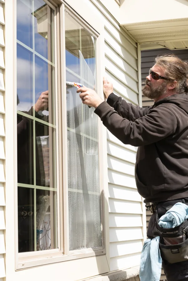Matt Bertsch squeegeeing an exterior window on a residential home, blue sky reflected in the glass
