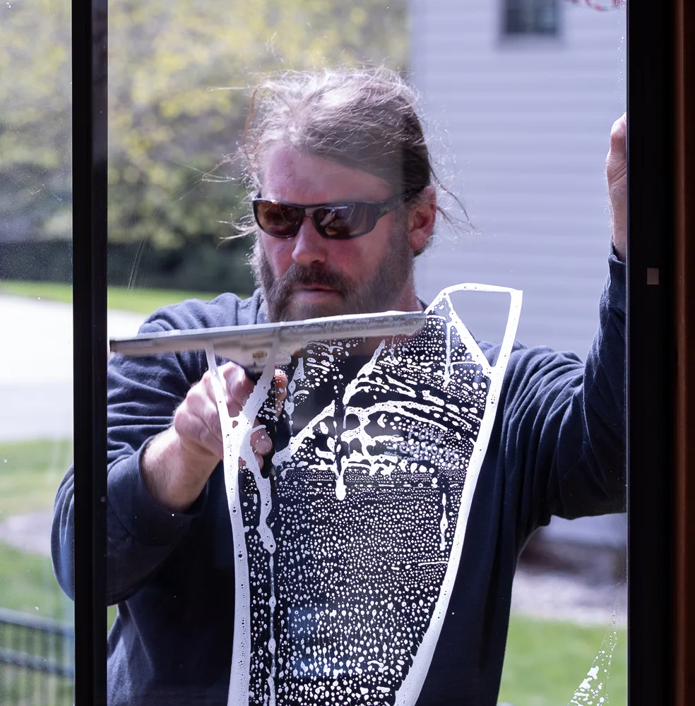 Matt Bertsch squeegeeing a window, photographed through the beading water on the glass